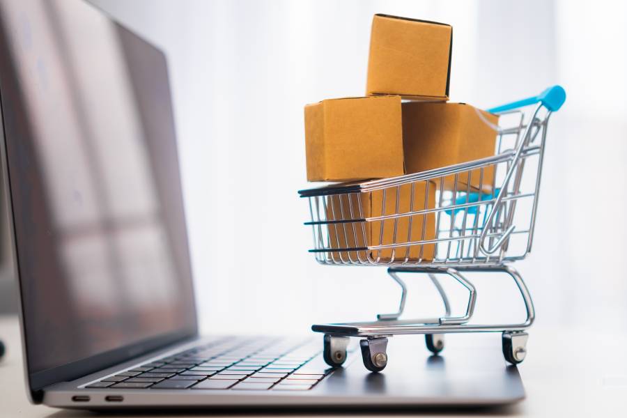 Carrito de compras en miniatura con cajas sobre laptop, representando el proceso de vender en marketplace de forma online