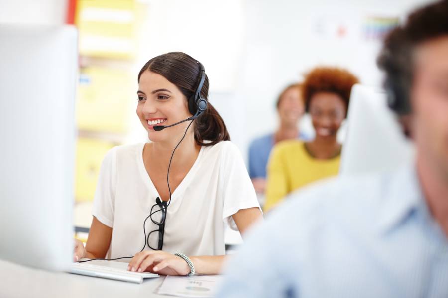 Agente de atención al cliente con IA sonriendo frente a computadora en centro de soporte