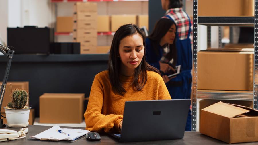 Mujer con suéter naranja trabajando en laptop, comparando ANYTOOLS vs Producteca  