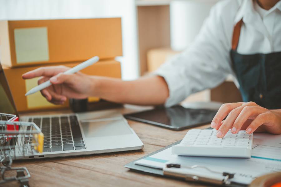 Vendedor usando calculadora y laptop para gestionar costos al anunciar en Mercado Libre 