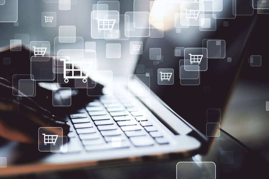 Manos sobre laptop con íconos de carrito flotantes, representando plataformas de ventas online en ecommerce. 