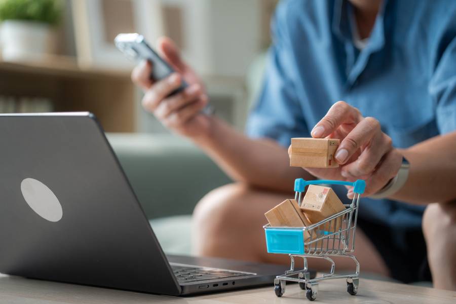 Miniatura de carrito de compras con cajas junto a laptop y smartphone, ilustrando hub de marketplaces multicanal 