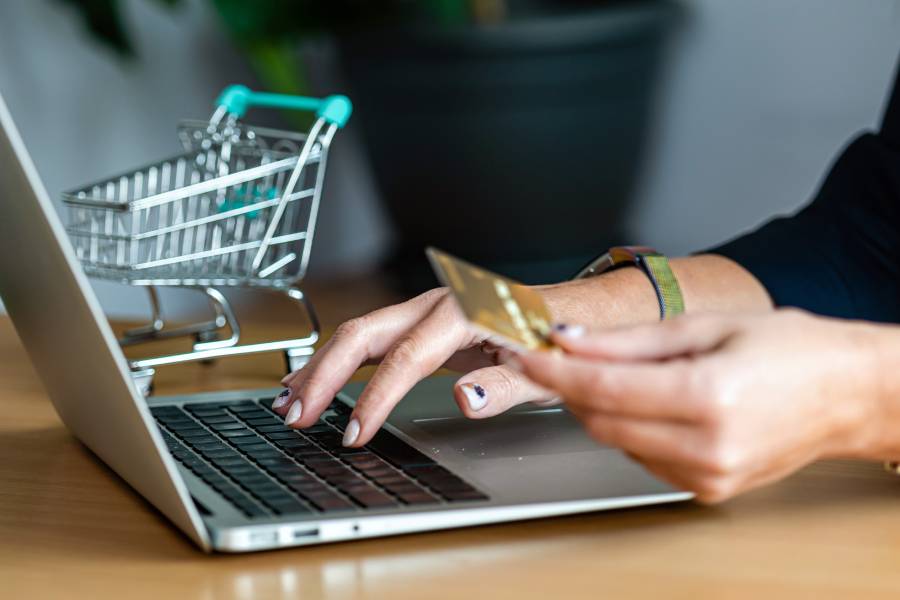 Persona realizando ventas en marketplaces desde laptop con tarjeta de crédito y carrito de compras en miniatura 